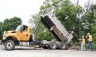 A dump truck is dumping dirt on the road.