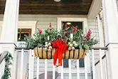 A person in red is sitting on the railing of a porch.