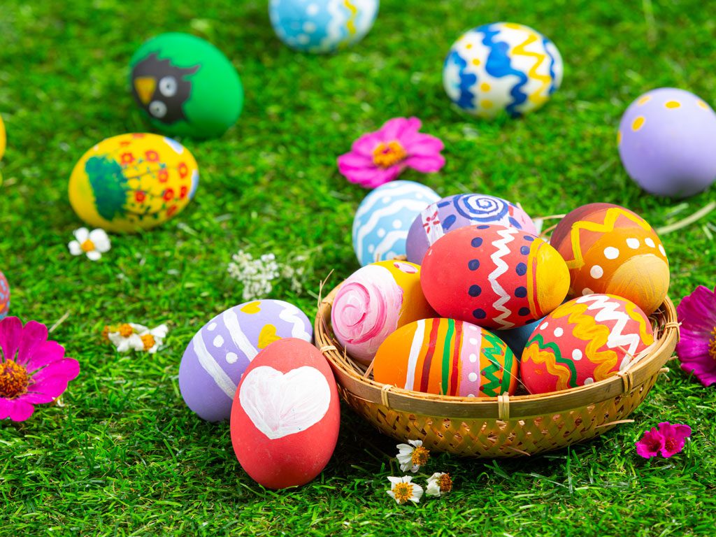 A basket of colorful eggs on the grass.