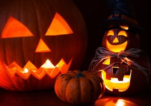 A group of lit candles sitting next to some pumpkins.